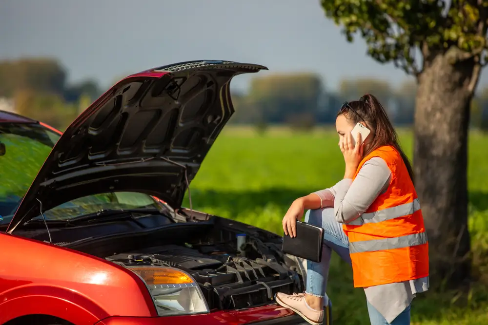 Žena vo veste pri aute pozerá do motora